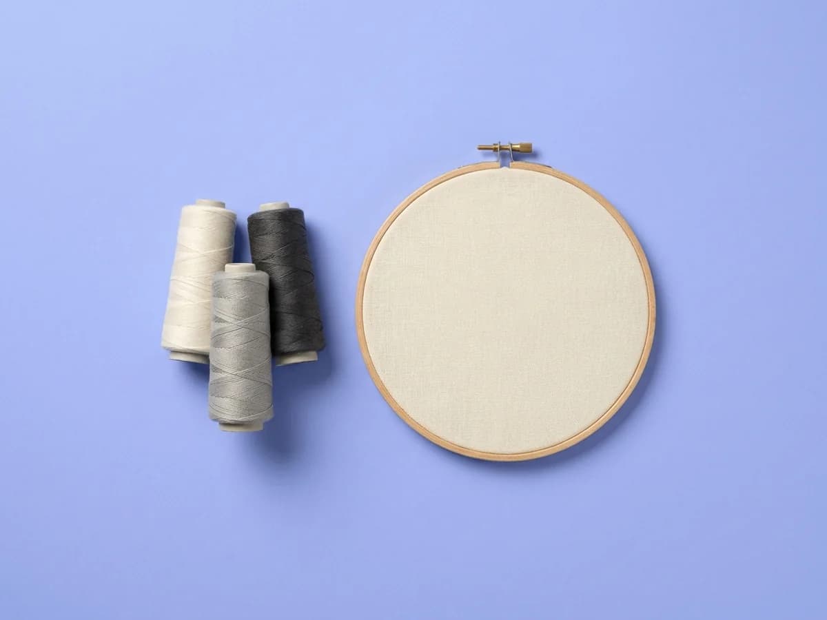 Thread cones beside an embroidery hoop holding blank fabric